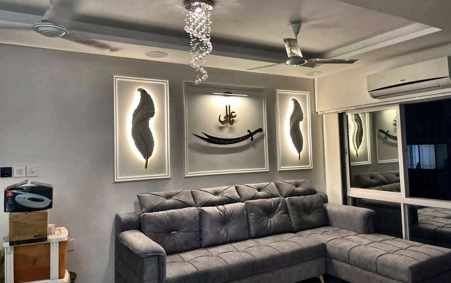 Living room in Goregaon West designed by Eminence Living with a grey L-shaped sofa, backlit wall panels and a cove-lit false ceiling