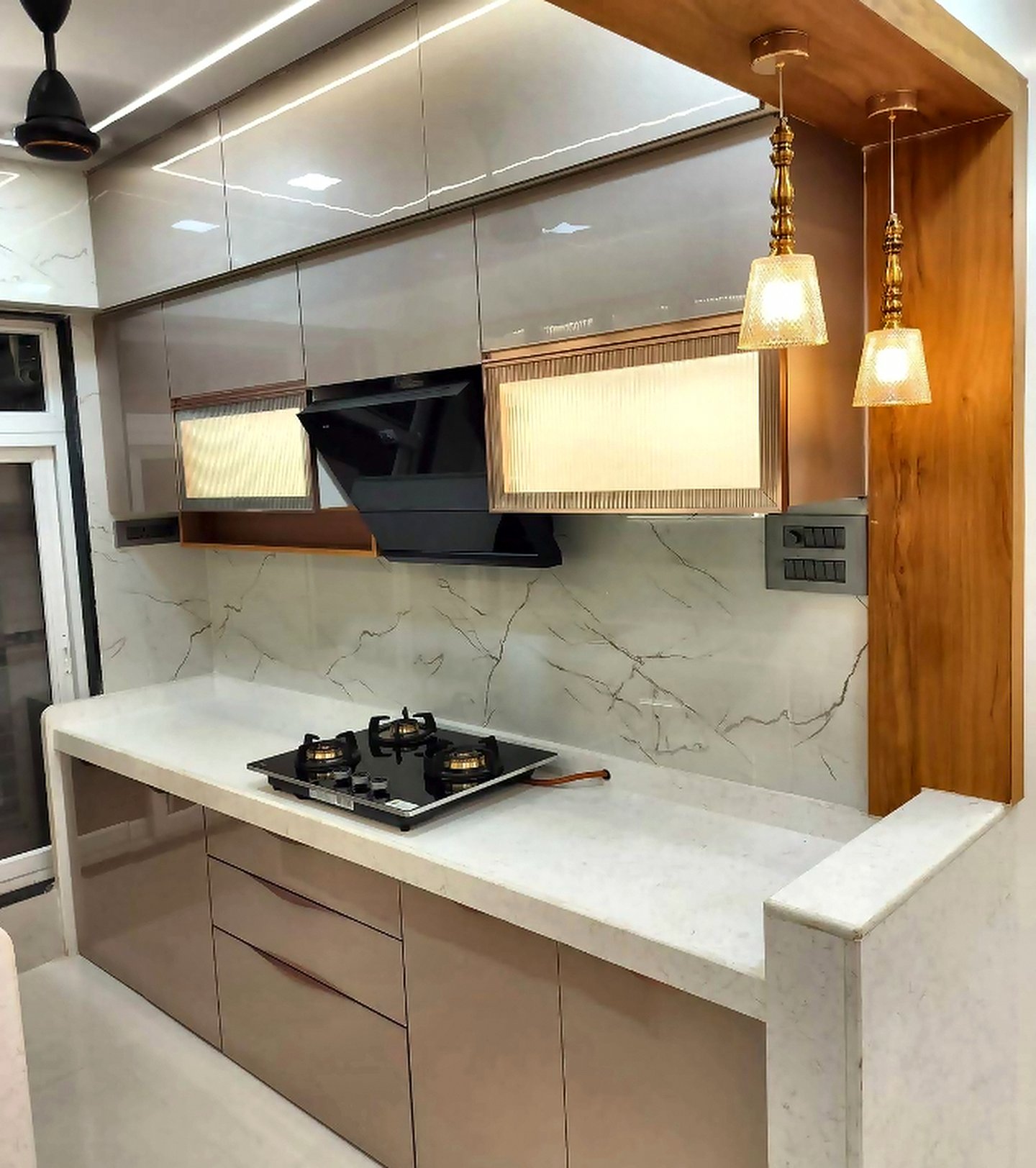 Beige modular kitchen with pendant lights, marble backsplash and a wall chimney